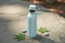 Charger l'image dans la galerie, Gourde bleue clair TREKKER'S ouverte posée sur une pierre avec feuilles vertes et galets