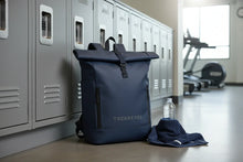 Charger l'image dans la galerie, Sac à dos bleu TREKKERSS posé au sol près des casiers gris dans un vestiaire de gym avec serviette et bouteille d'eau
